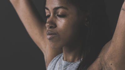 A woman with a relaxed face and closed eyes hold both arms above her head.